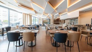 A modern dining area with tables and chairs, large windows, and a kitchen in the background. - Jupiter Porto Hotel - Rooftop & Spa (Porto)