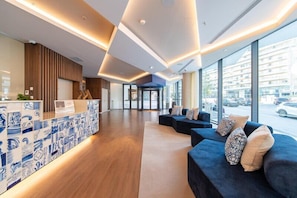 A modern hotel lobby with a reception desk, seating area, and large windows.