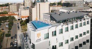 A modern hotel with a rooftop pool, a prominent 'Jupiter Porto' sign, and a view of the surrounding cityscape. - Jupiter Porto Hotel - Rooftop & Spa (Porto)
