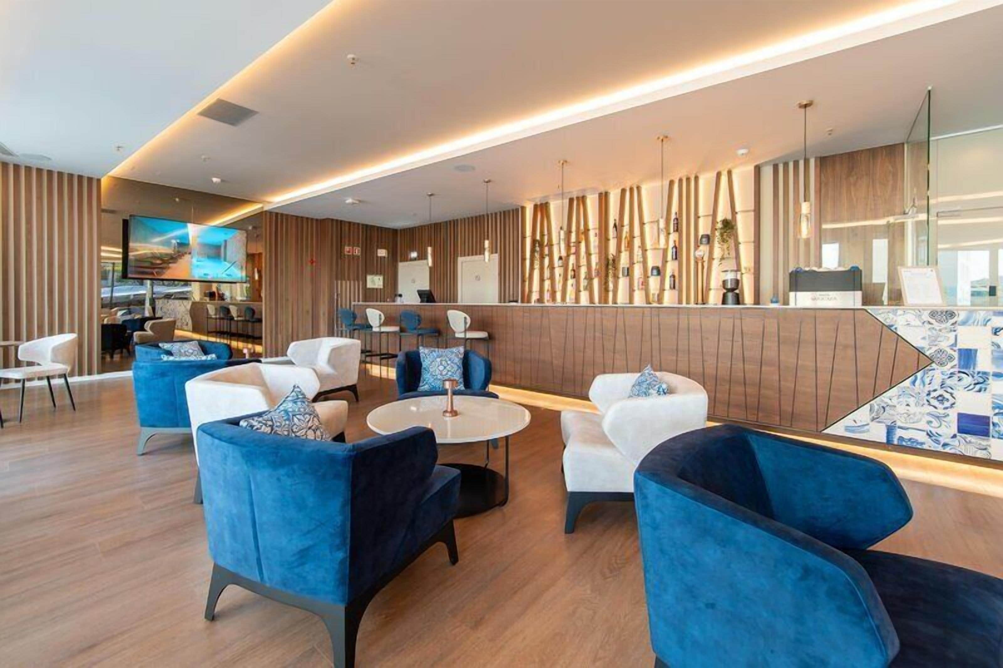 A modern hotel lobby with seating areas, a reception desk, and a bar.