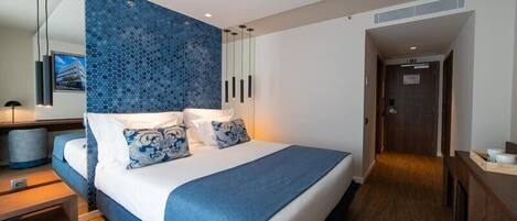 A modern hotel room with a large bed, a desk, and a view of the city.