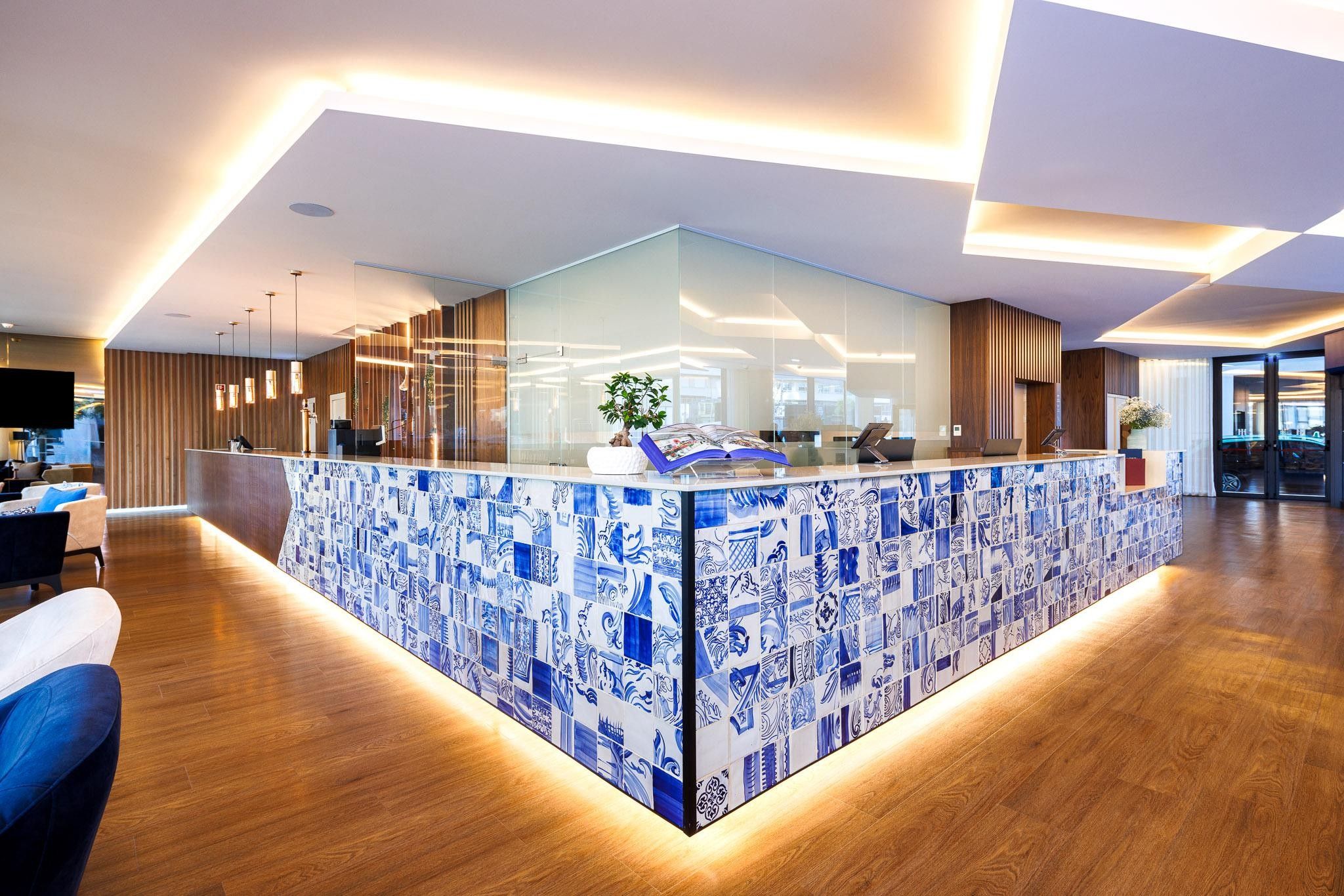 Un espace d’accueil doté d’une cloison en verre, d’un plancher en bois et d’un mur recouvert de carreaux aux motifs bleus.