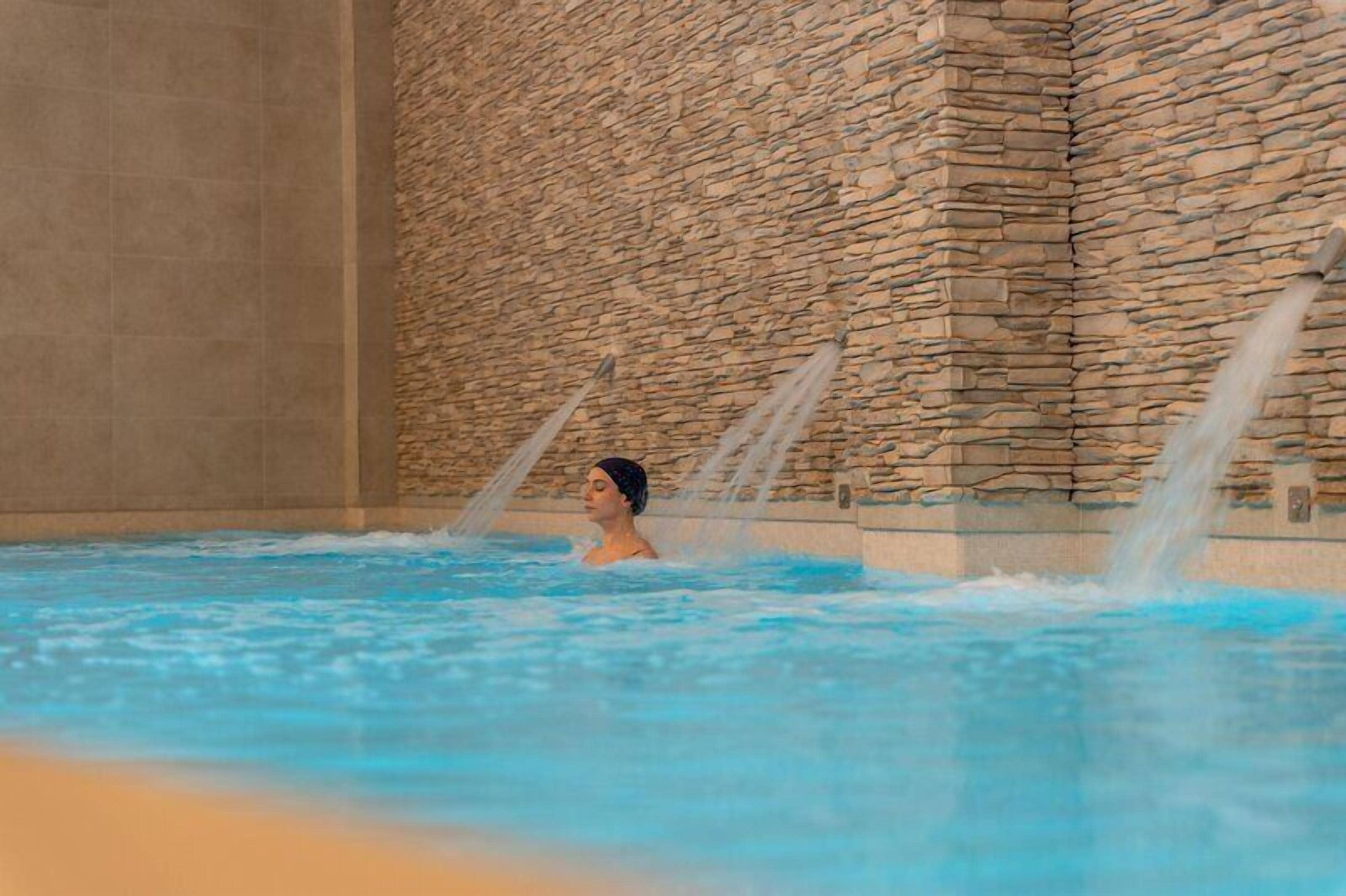 Una persona en una piscina con paredes de piedra y chorros de agua.