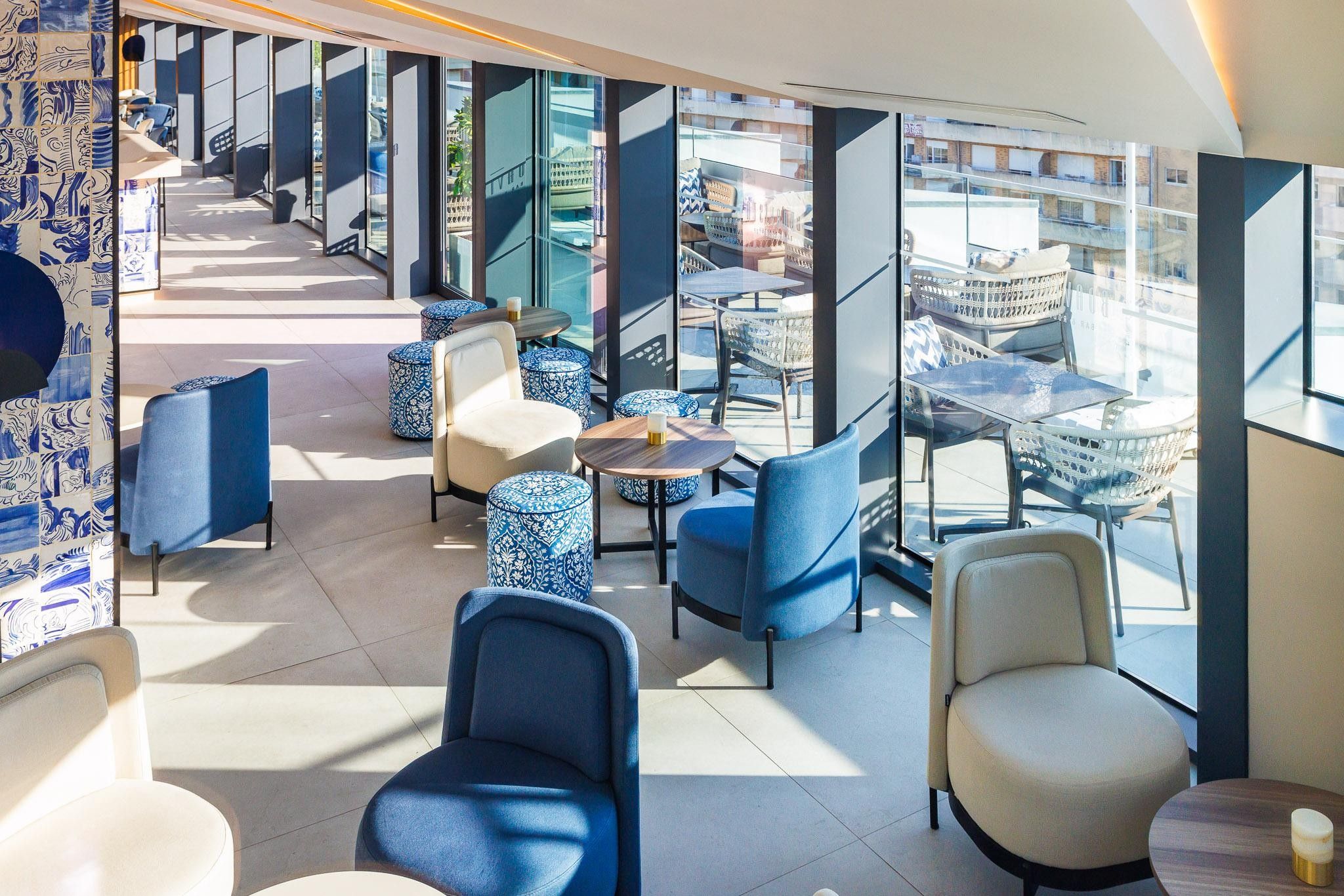 A modern lounge area with seating and tables, large windows, and a view of the city.