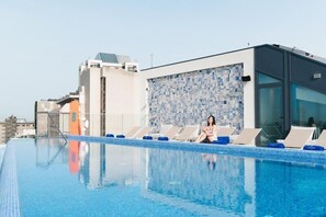Una piscina sul tetto con un muro piastrellato, poltrone relax e una struttura di un edificio moderno.