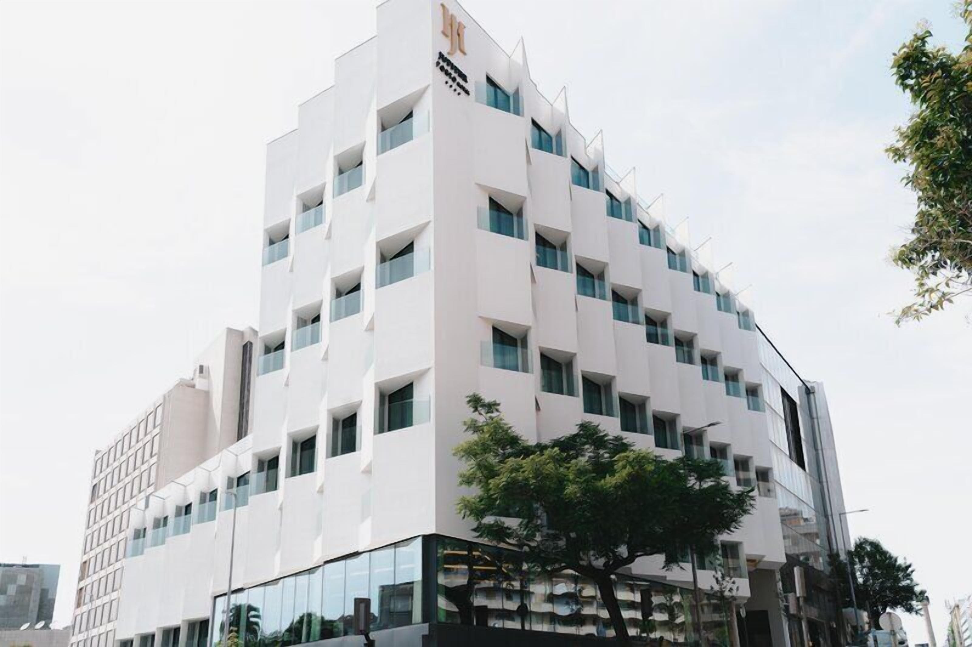 Un edificio moderno con fachada blanca, múltiples ventanales y un árbol en primer plano.