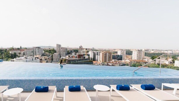 A rooftop infinity pool with lounge chairs and a cityscape view. - Jupiter Porto Hotel - Rooftop & Spa (Porto)
