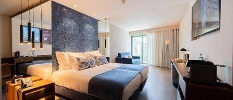 A modern hotel room with a large bed, a desk, and a view of the city.
