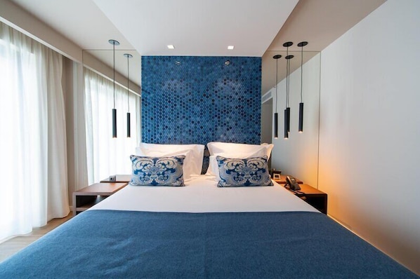 A modern hotel room with a large bed, two bedside tables, a blue patterned wall, and pendant lights. - Jupiter Porto Hotel - Rooftop & Spa (Porto)