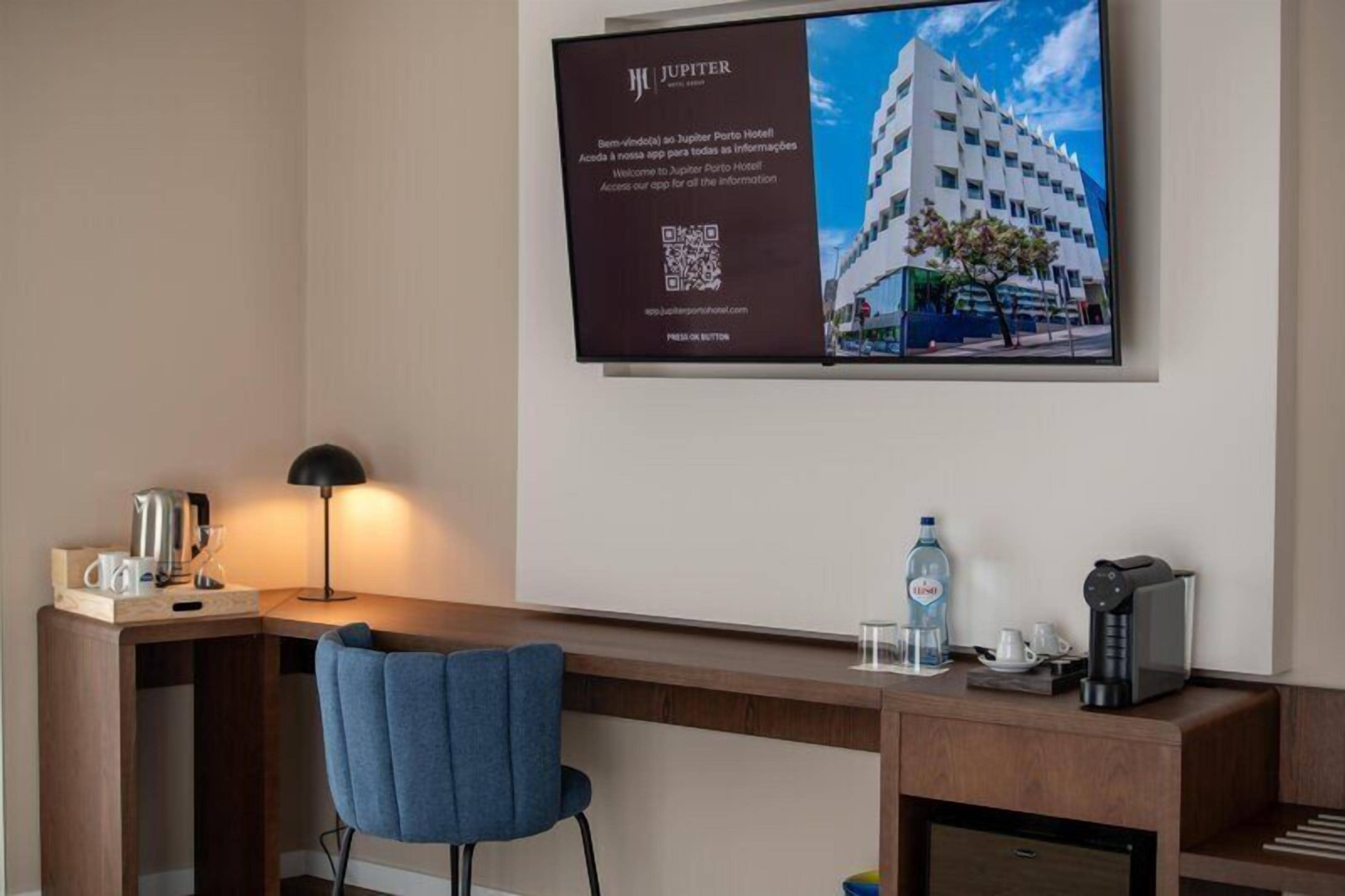 A hotel room with a desk, chair, lamp, and a large poster of a building.