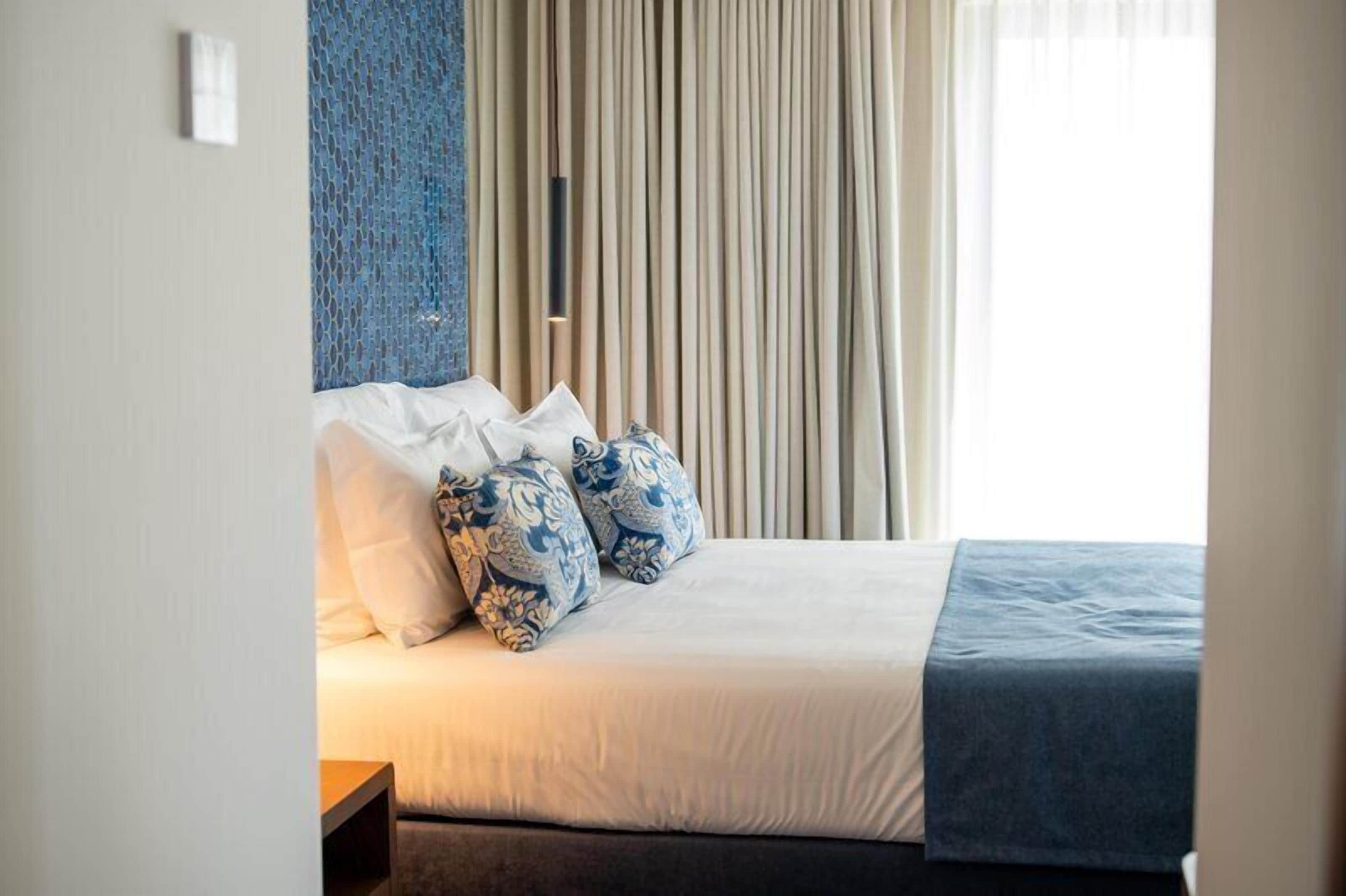 Quarto de hotel com cama, almofadas, cortinas e parede com textura.