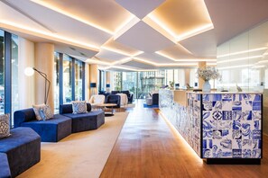 A modern hotel lobby with seating areas, a reception desk, and large windows offering views.