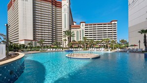 Un área de piscina hotelera con múltiples sillas de descanso y sombrillas, rodeada de edificios altos.