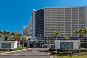 Ein modernes Hotel mit einer geschwungenen Glasfassade, einem Parkhauszugang und Palmen im Vordergrund.