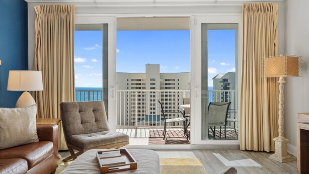 Habitación de hotel con balcón, sofá, una silla, una mesa y una lámpara.