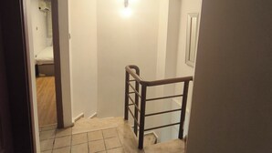 Un pasillo estrecho con suelo de baldosas, barandilla de madera y una lámpara en la pared.