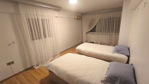 Una habitación pequeña y limpia con dos camas, suelo de madera y paredes blancas.