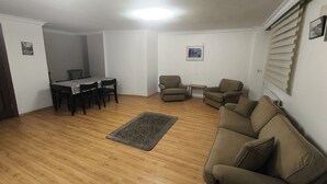 Una sala de estar con piso de madera, un sofá marrón, una mesa de comedor con sillas y una mesita auxiliar.