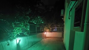 Un estrecho pasillo exterior con suelo de hormigón, una pequeña mesa y una lámpara fijada a la pared.