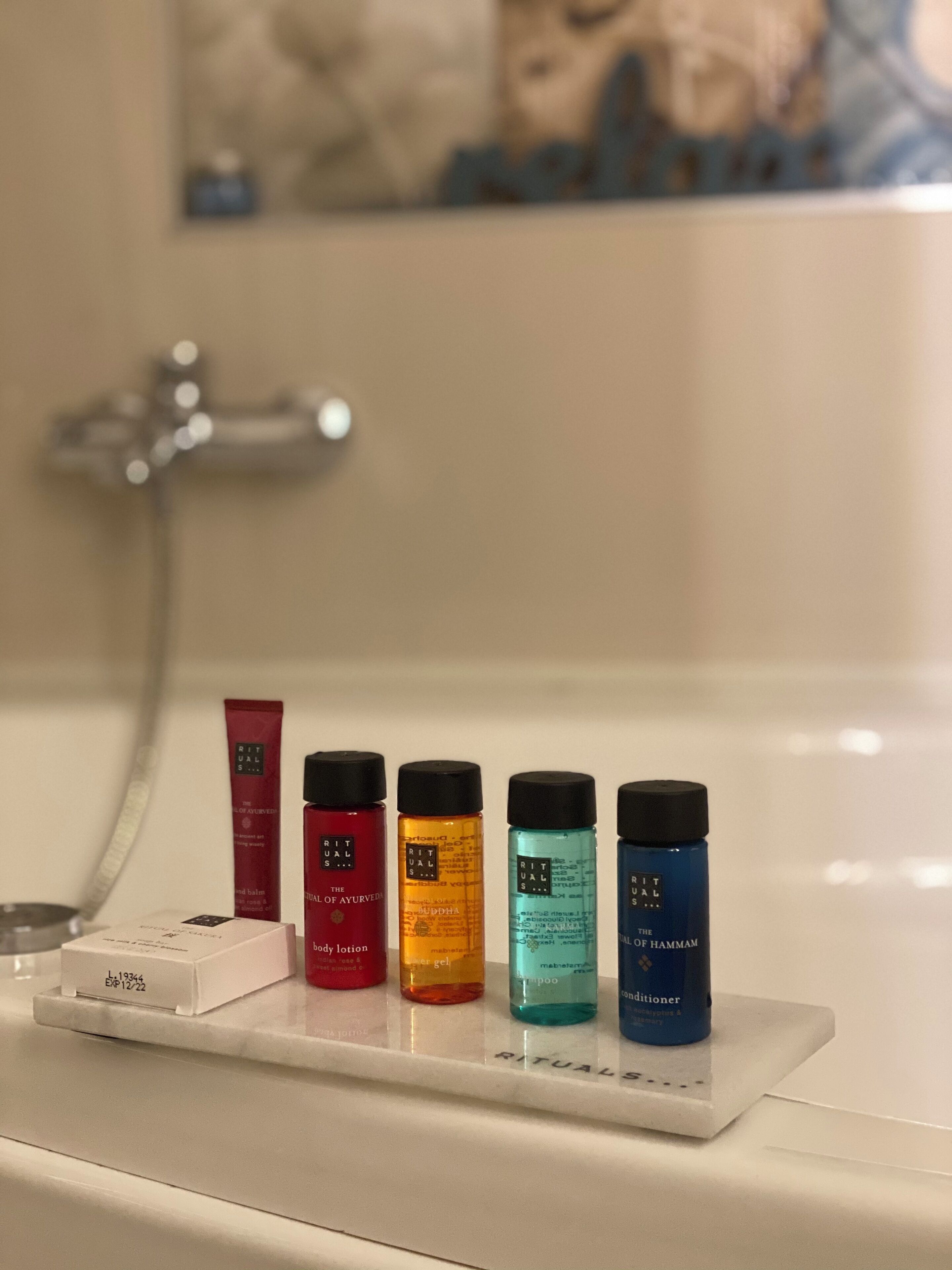 A bathroom with a white sink and a mirror. On the sink, there are five bottles of Rituals body lotion, arranged in a row.