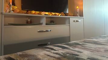 Quarto moderno com televisão de tela plana na parede, cama com colcha estampada e mesa de cabeceira com uma vela.