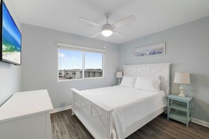 Ein Schlafzimmer mit einem Bett, einem Nachttisch, einem Deckenventilator, einem Fenster mit Blick und einem an der Wand montierten Fernseher.