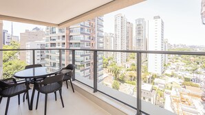 Un balcon doté d’une table et de chaises en verre, offrant une vue sur les gratte-ciel et le paysage urbain.