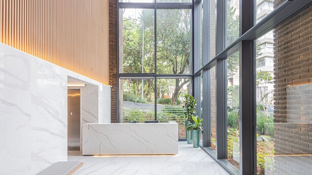 Un espace d’accueil moderne, doté d’un comptoir de réception en marbre, de grandes fenêtres offrant une vue sur la verdure, et d’un mélange de murs en briques et de lambris en bois.