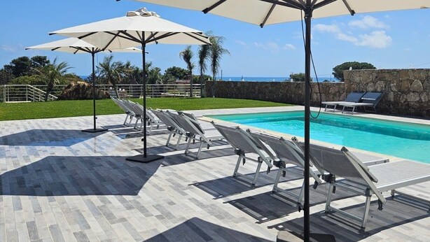 A poolside area with lounge chairs and umbrellas, a stone wall, and a clear view of the ocean. - Cava Del Mar: comfort and relaxation in a vacation home with bedroom, living room and bathroom. (Augusta)