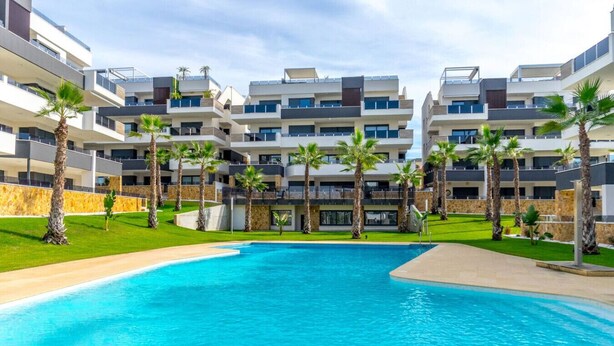 Un hotel moderno con piscina central, varios balcones y palmeras.