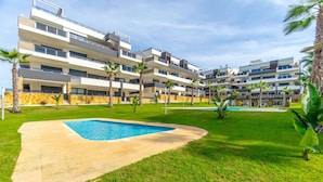Un hotel moderno de varios pisos con piscina, palmeras y un césped bien cuidado.