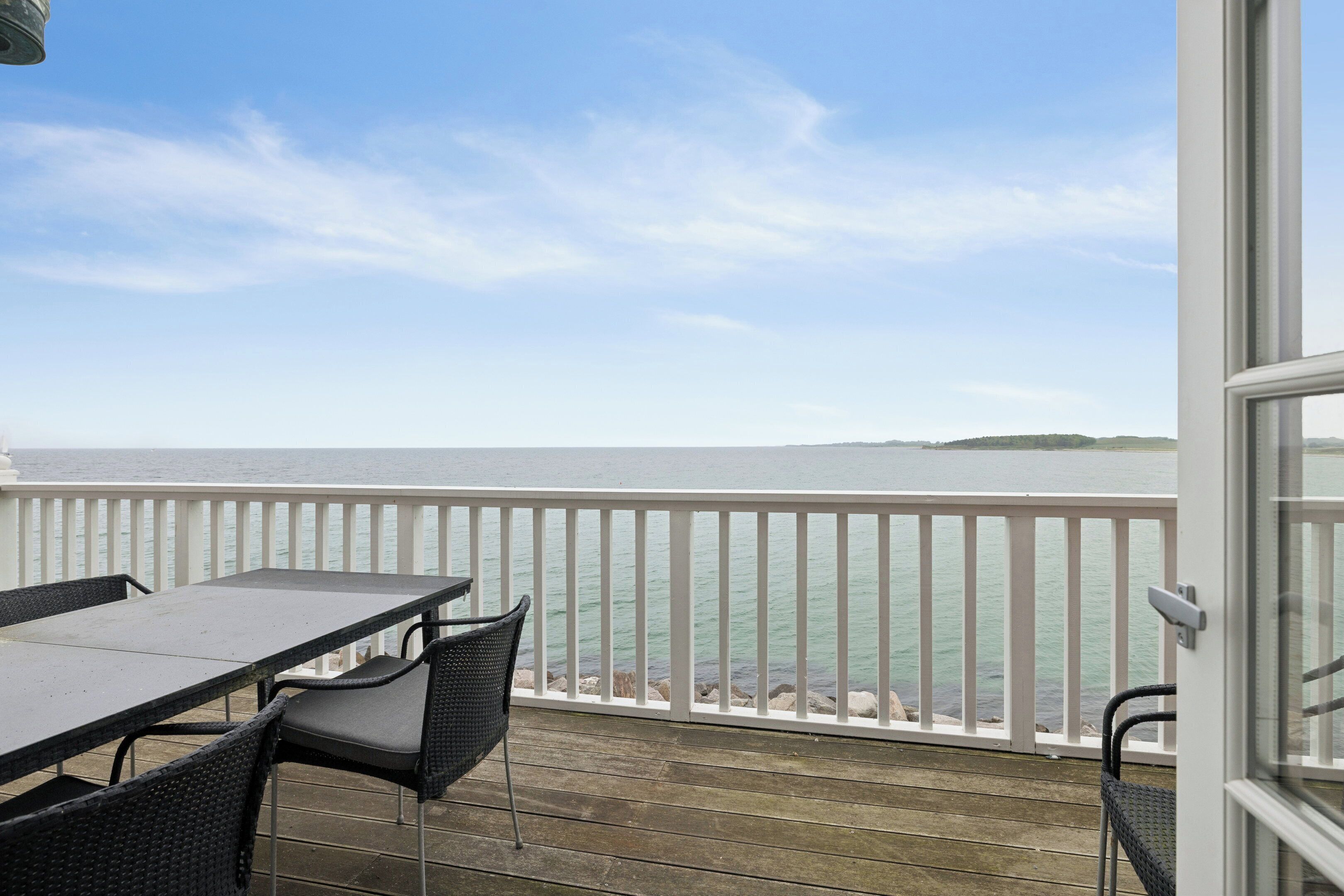A balcony with a table and chairs, overlooking a body of water and a distant landmass.