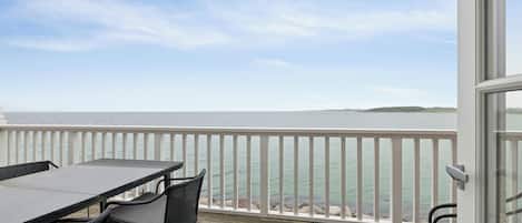 A balcony with a table and chairs, overlooking a body of water and a distant landmass.