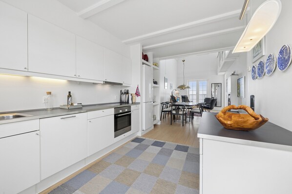 Et moderne køkken med hvide skabe, en central ø og et spiseområde med bord og stole.