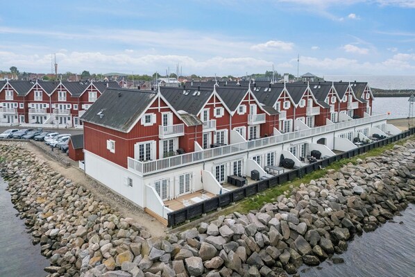 A row of red and white buildings with balconies, a rocky shoreline, and a calm body of water in the background. - Appartment by the sea and family friendly beach (Bagenkop)