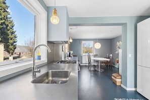 A modern kitchen with a large window, stainless steel appliances, and a dining area with a table and chairs. - Spacious holiday home on a large natural plot (Nexø)