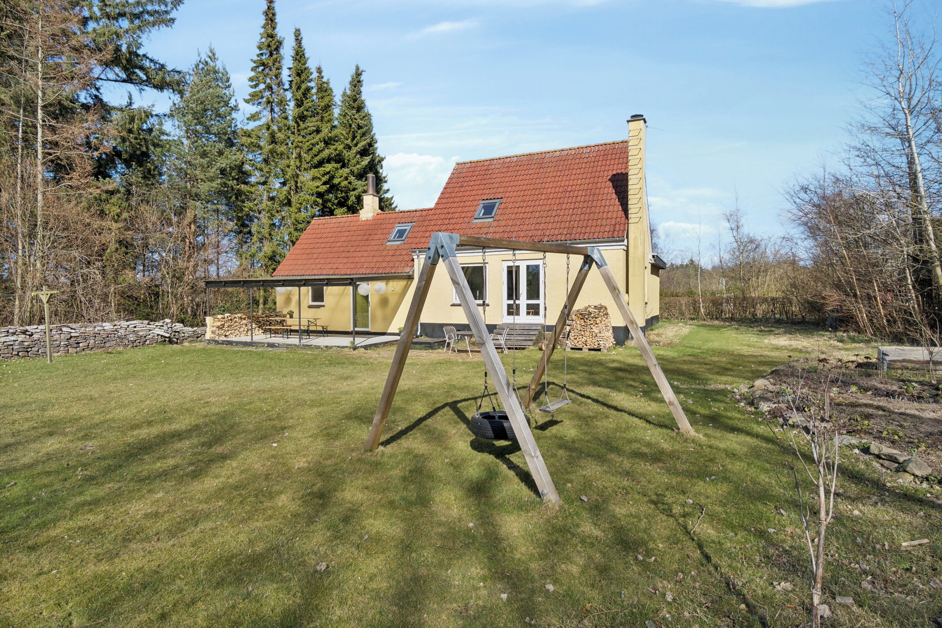 A house with a red-tiled roof, a swing set, and a stone wall in a grassy yard.