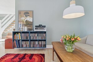 A living room with a bookshelf, a coffee table with a vase of flowers, and a large pendant light. - Spacious holiday home on a large natural plot (Nexø)