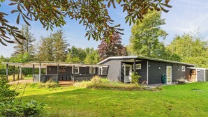 Een gebouw met twee verdiepingen, een overdekt terras, een klein houten terras en een verzorgd gazon.