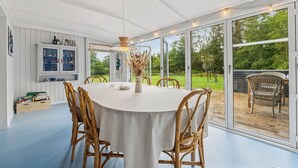 Een eetruimte met een ronde tafel, stoelen en uitzicht door grote glazen deuren op een terras.