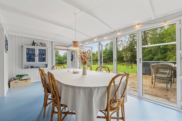 A dining area with a round table, chairs, and a view through large glass doors to an outdoor deck.