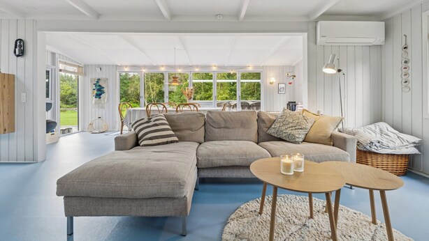 Een moderne woonkamer met een modulaire bank, een ronde houten salontafel en uitzicht op groen door grote ramen.