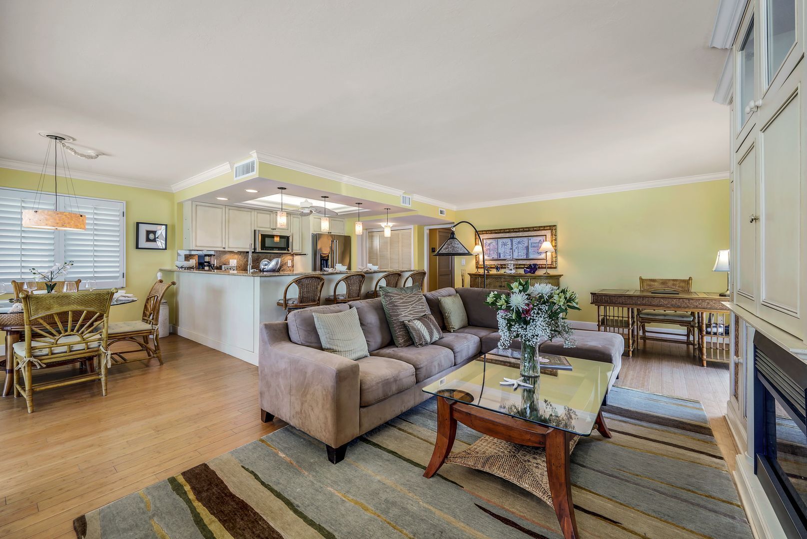 A spacious living room with a sofa, a glass coffee table, and a dining area with wicker chairs.