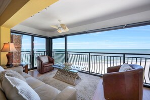 Un vaste balcon offrant une vue sur l’océan, aménagé avec des fauteuils en cuir et une table en verre.