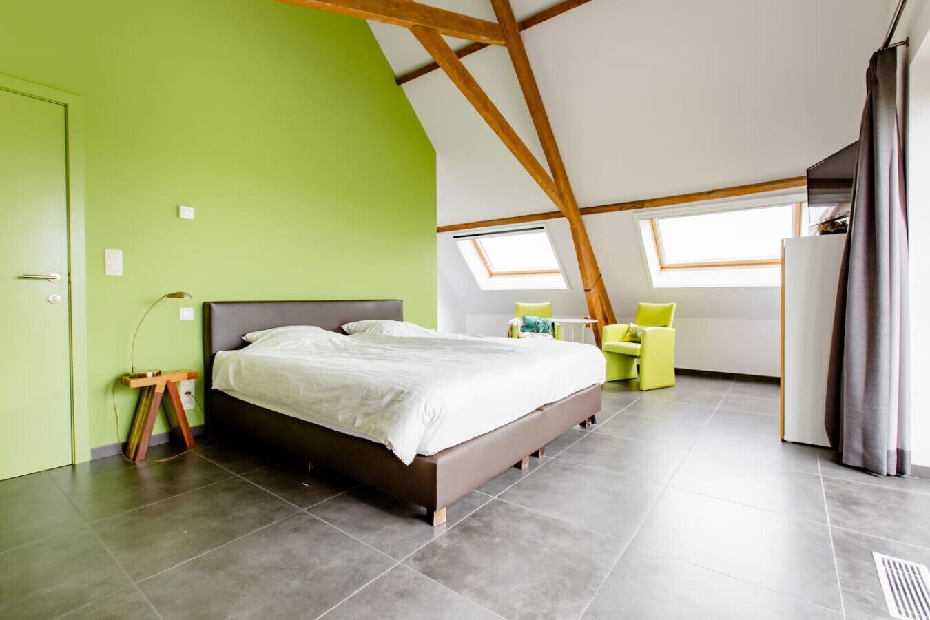 Un dormitorio moderno con una cama grande, ventanas de tragaluz y una pared de acento verde.
