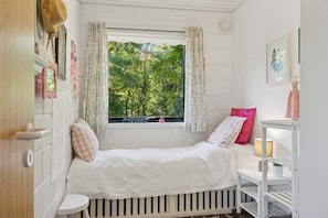 A small, cozy bedroom with a single bed, a window with curtains, a bedside table with a lamp, and a wall-mounted shelf. - Holiday home with pool, terraces, near beach (Sjællands Odde)