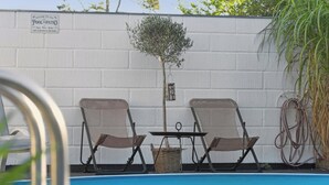 Un espace piscine comprenant deux chaises, une table et un panneau indiquant : « Bienvenue dans notre espace piscine-terrasse. »