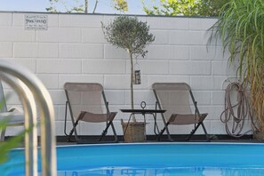 Ein Poolbereich mit zwei Stühlen, einem Tisch und einem Schild mit der Aufschrift 'Welcome to our Pool-Patio'.