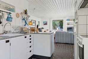 A kitchen with white cabinetry, a granite countertop, and a brick floor. - Holiday home with pool, terraces, near beach (Sjællands Odde)
