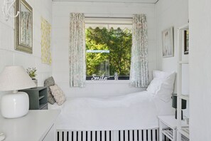 Ein Schlafzimmer mit Bett, Nachttisch, Lampe, einem Fenster mit Vorhängen und einem Wandspiegel.